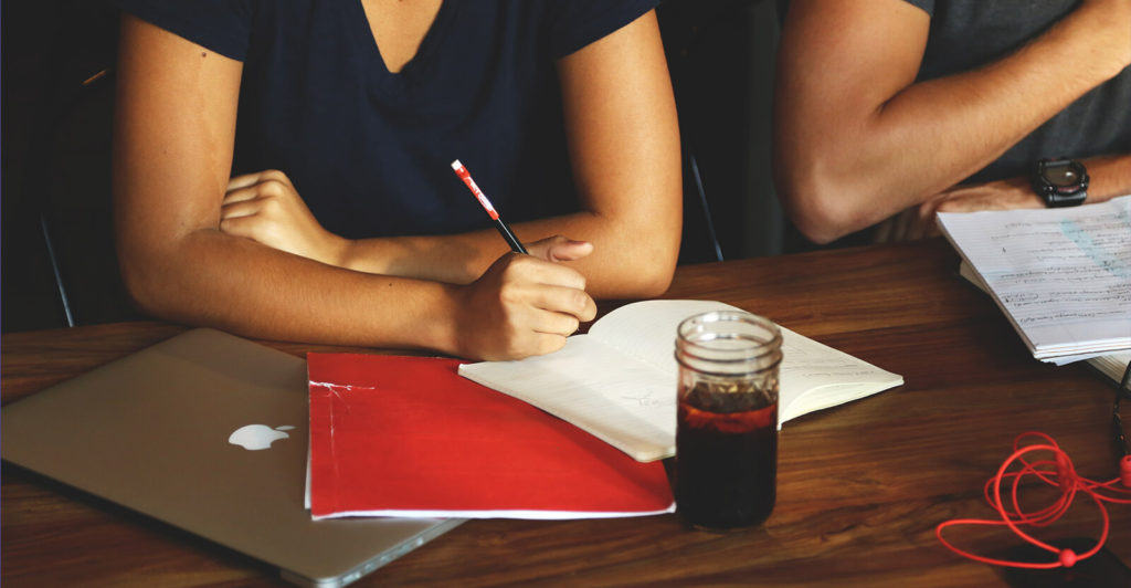 Two people sitting at a desk and writing on a notebook